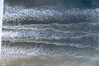 a surfer on an ocean wave rolls around in the distance with the surfboard in focus