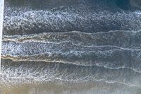 a surfer on an ocean wave rolls around in the distance with the surfboard in focus