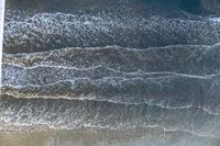 a surfer on an ocean wave rolls around in the distance with the surfboard in focus