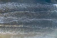 a surfer on an ocean wave rolls around in the distance with the surfboard in focus