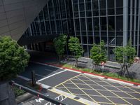 a parking lot with cars driving next to a large building with glass walls and many trees around the structure