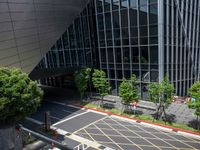 a parking lot with cars driving next to a large building with glass walls and many trees around the structure