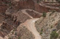 a truck driving down a mountainous canyon side road with its front wheel down on a steep cliff