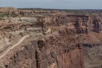 a canyon with rocks, shrubs and trees near by on a dirt road passing through them