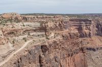 a canyon with rocks, shrubs and trees near by on a dirt road passing through them