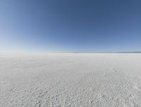 a view looking down a snow field to an island of land beyond the horizon with a jet trail in the distance