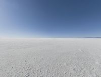 a view looking down a snow field to an island of land beyond the horizon with a jet trail in the distance