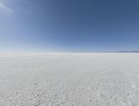 a view looking down a snow field to an island of land beyond the horizon with a jet trail in the distance