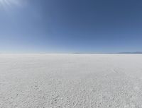 a view looking down a snow field to an island of land beyond the horizon with a jet trail in the distance