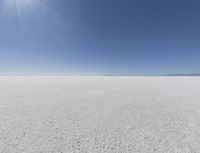 a view looking down a snow field to an island of land beyond the horizon with a jet trail in the distance