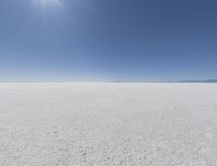 a view looking down a snow field to an island of land beyond the horizon with a jet trail in the distance