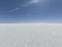 a view looking down a snow field to an island of land beyond the horizon with a jet trail in the distance