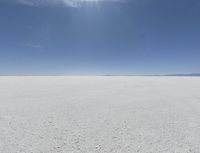 a view looking down a snow field to an island of land beyond the horizon with a jet trail in the distance