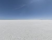 a view looking down a snow field to an island of land beyond the horizon with a jet trail in the distance