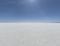 a view looking down a snow field to an island of land beyond the horizon with a jet trail in the distance