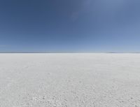 a view looking down a snow field to an island of land beyond the horizon with a jet trail in the distance