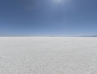 a view looking down a snow field to an island of land beyond the horizon with a jet trail in the distance