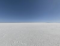 a view looking down a snow field to an island of land beyond the horizon with a jet trail in the distance