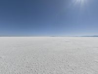 a view looking down a snow field to an island of land beyond the horizon with a jet trail in the distance