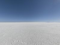 a view looking down a snow field to an island of land beyond the horizon with a jet trail in the distance