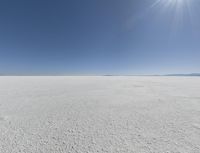 a view looking down a snow field to an island of land beyond the horizon with a jet trail in the distance