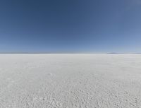 a view looking down a snow field to an island of land beyond the horizon with a jet trail in the distance