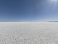 a view looking down a snow field to an island of land beyond the horizon with a jet trail in the distance