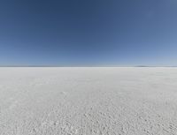 a view looking down a snow field to an island of land beyond the horizon with a jet trail in the distance