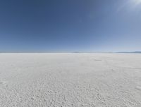 a view looking down a snow field to an island of land beyond the horizon with a jet trail in the distance