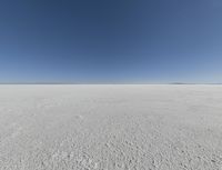 a view looking down a snow field to an island of land beyond the horizon with a jet trail in the distance