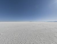 a view looking down a snow field to an island of land beyond the horizon with a jet trail in the distance