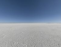 a view looking down a snow field to an island of land beyond the horizon with a jet trail in the distance