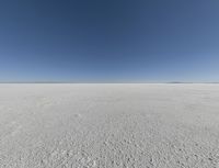 a view looking down a snow field to an island of land beyond the horizon with a jet trail in the distance