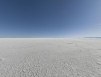 a view looking down a snow field to an island of land beyond the horizon with a jet trail in the distance