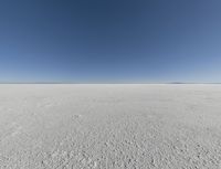 a view looking down a snow field to an island of land beyond the horizon with a jet trail in the distance