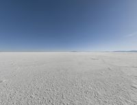 a view looking down a snow field to an island of land beyond the horizon with a jet trail in the distance