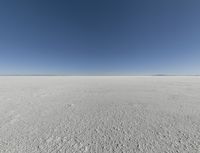 a view looking down a snow field to an island of land beyond the horizon with a jet trail in the distance