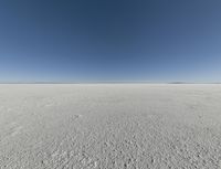 a view looking down a snow field to an island of land beyond the horizon with a jet trail in the distance