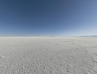 a view looking down a snow field to an island of land beyond the horizon with a jet trail in the distance