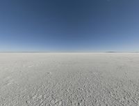 a view looking down a snow field to an island of land beyond the horizon with a jet trail in the distance