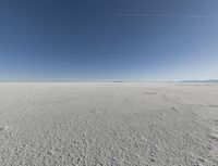 a view looking down a snow field to an island of land beyond the horizon with a jet trail in the distance