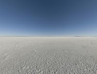 a view looking down a snow field to an island of land beyond the horizon with a jet trail in the distance