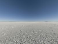 a view looking down a snow field to an island of land beyond the horizon with a jet trail in the distance