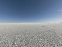 a view looking down a snow field to an island of land beyond the horizon with a jet trail in the distance