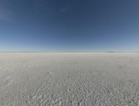 a view looking down a snow field to an island of land beyond the horizon with a jet trail in the distance