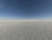 a view looking down a snow field to an island of land beyond the horizon with a jet trail in the distance