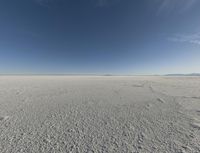 a view looking down a snow field to an island of land beyond the horizon with a jet trail in the distance