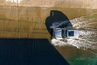 an overhead view of a white car driving down the road near the water's edge