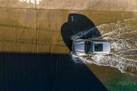 an overhead view of a white car driving down the road near the water's edge