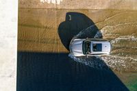 an overhead view of a white car driving down the road near the water's edge